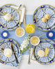 Table setting with blue and white patterned plates, cutlery, and small dishes on a light blue tablecloth.