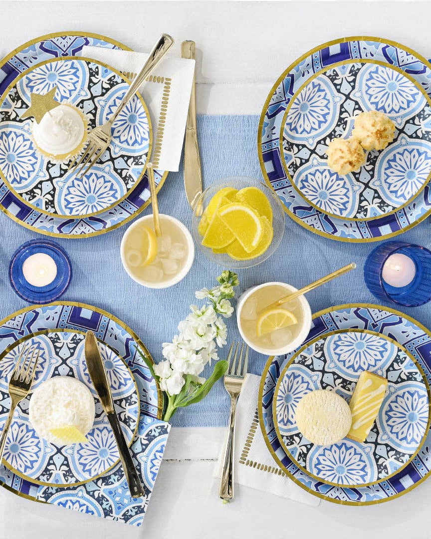 Table setting with blue and white patterned plates, cutlery, and small dishes on a light blue tablecloth.